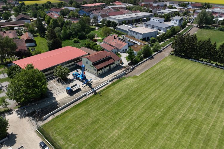Am Sportplatz wurden in einen Teil der Schutzmauer kleine Sitzstufen eingebaut. Drohnenaufnahme vom 14.05.2025